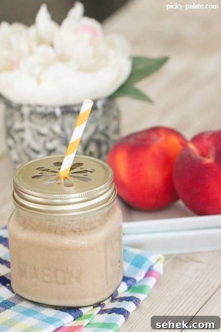 Essential Summer Drinks You Need This Season 9 A peaches and cream frosty in a glass mug with a lid and a yellow-striped straw.