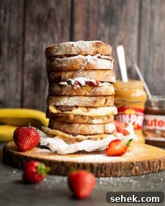 4 sandwiches stacked on each other on wooden board garnished with icing sugar and strawberries