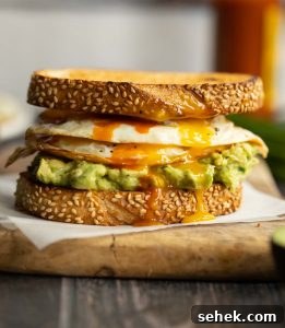 sandwich on parchment paper on chopping board with chives, hot sauce and eggs blurred in background