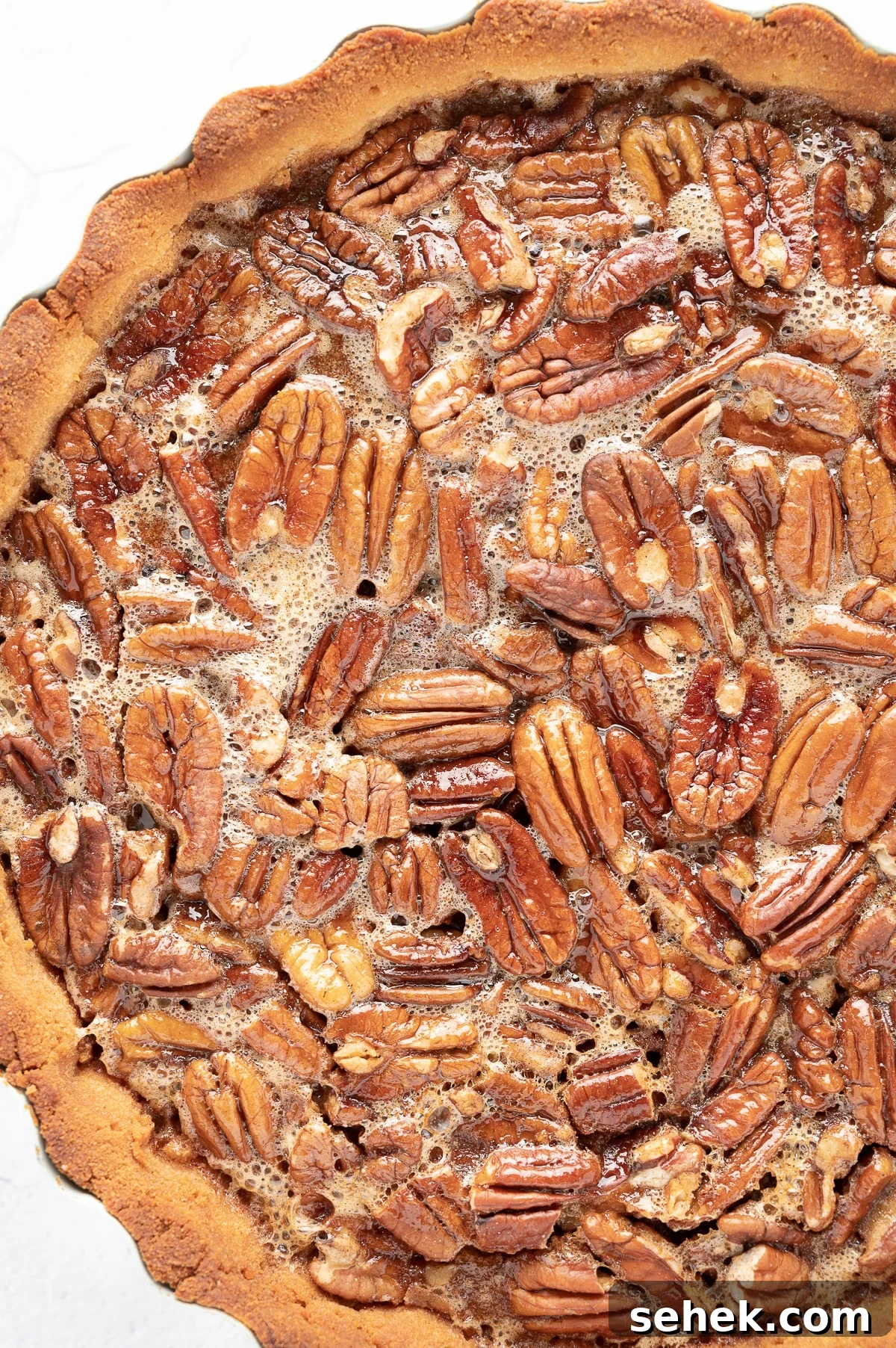 Sticky Sugar-Free Pecan Pie That Stays Gooey Even When Cold 4 a close up image of the top of a pecan pie showing the sticky gooey texture of the filling and golden baked pecans in a perfectly baked crust.