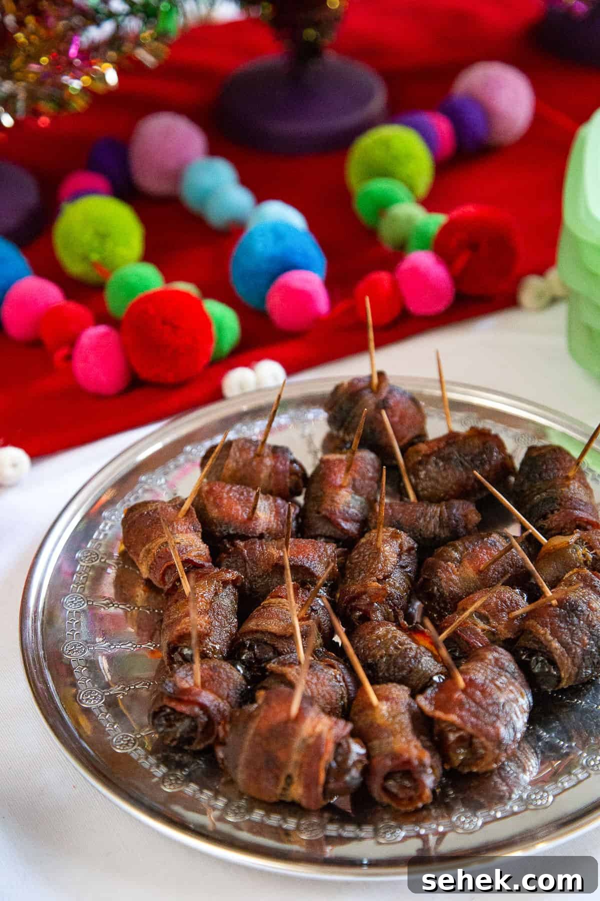 Bourbon Bacon-Wrapped Dates: Sweet, Savory Party Bites 2 boozy bacon wrapped dates secured with toothpicks on a metal plate, next to colorful pompom garland.