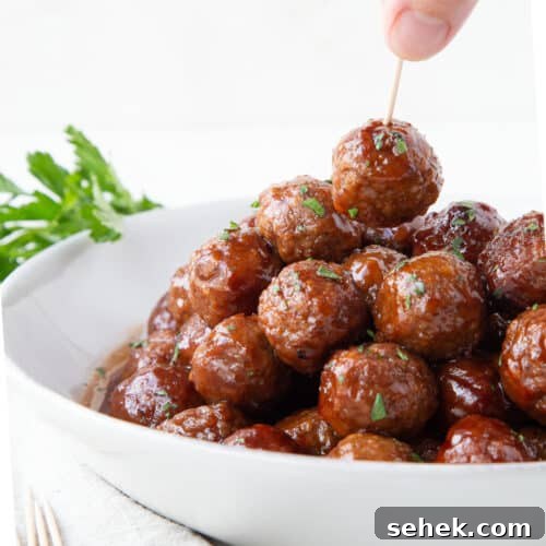 hand picking up a meatballs with a toothpick from a white bowl full of crockpot bbq meatballs.