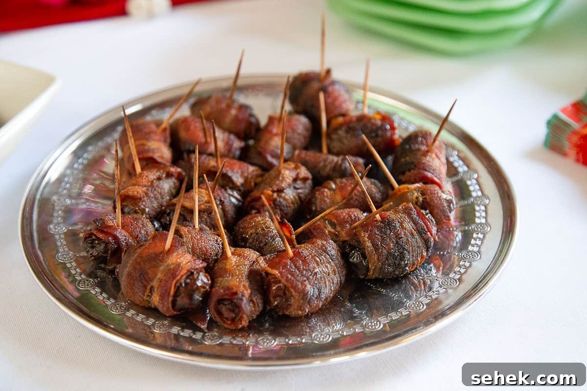Bourbon Bacon-Wrapped Dates: Sweet, Savory Party Bites 3 bacon wrapped dates on a round metal plate on a white tablecloth.