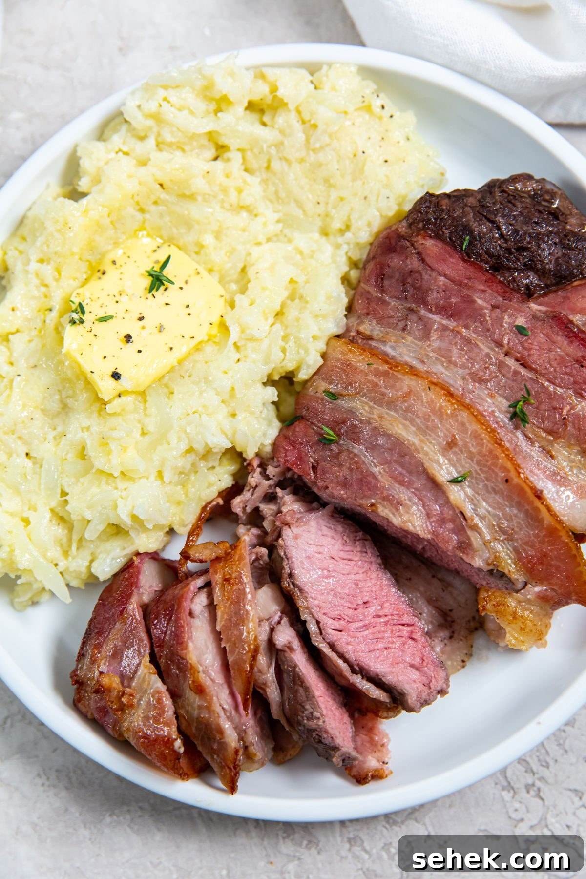 Air Fryer Bacon-Wrapped Ribeye Steak Recipe 2 Sliced Air fryer Bacon Wrapped Ribeye Steak with a side of cheesy mashed cauliflower on a white plate