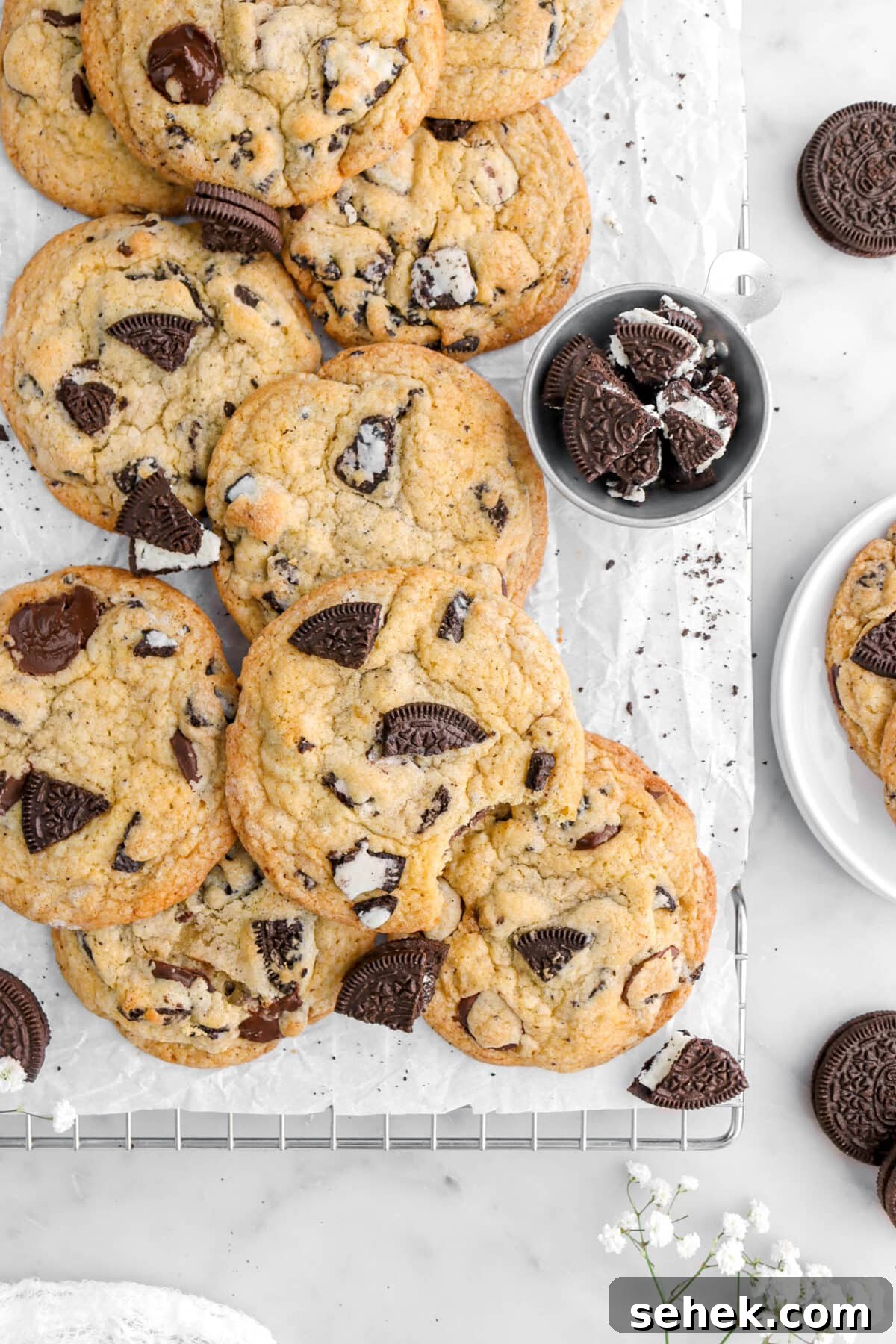 Oreo Chocolate Chip Cookies Recipe — Crispy Cookies with Oreo Chunks 2 cropped overhead shot of oreo chocolate chip cookies, with one cookie missing a bite on parchment lined cooling rack with oreos around.