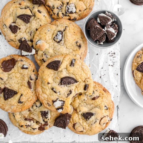 Oreo Chocolate Chip Cookies Recipe — Crispy Cookies with Oreo Chunks 12 cropped overhead shot of oreo chocolate chip cookies, with one cookie missing a bite on parchment lined cooling rack with oreos around.