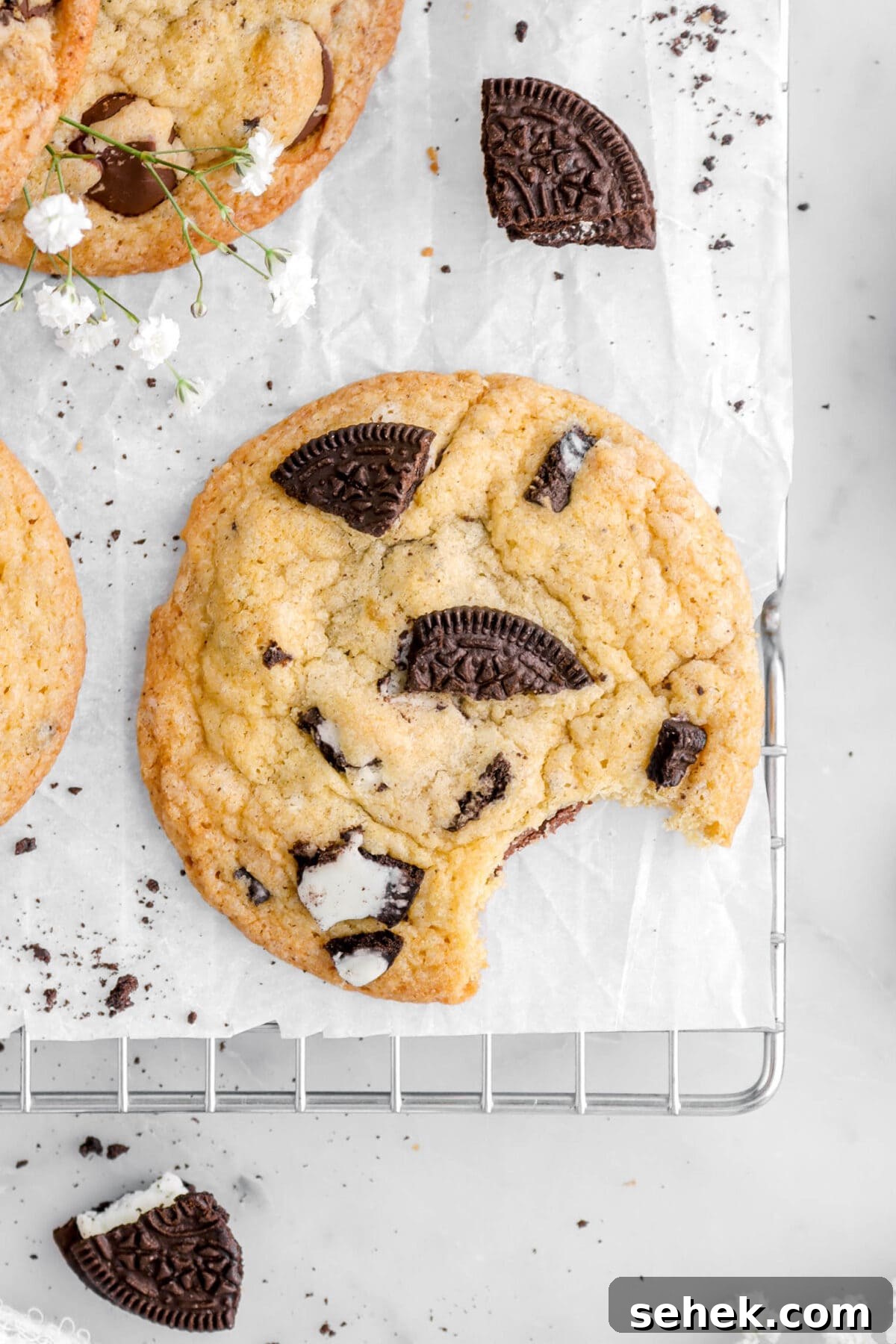 Oreo Chocolate Chip Cookies Recipe — Crispy Cookies with Oreo Chunks 3 close up overhead shot of oreo cookie with bite missing on parchment paper on cooling rack.