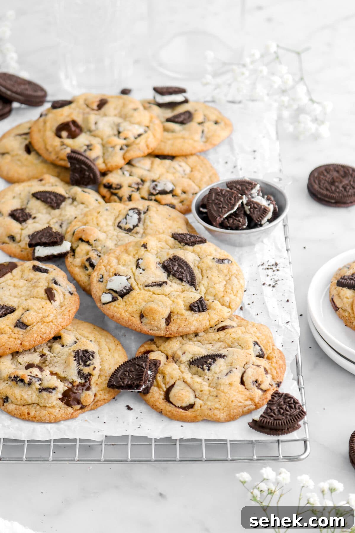 Oreo Chocolate Chip Cookies Recipe — Crispy Cookies with Oreo Chunks 4 angled cropped shot of cookies with oreos around on cooling rack lined with parchment paper with flowers around.