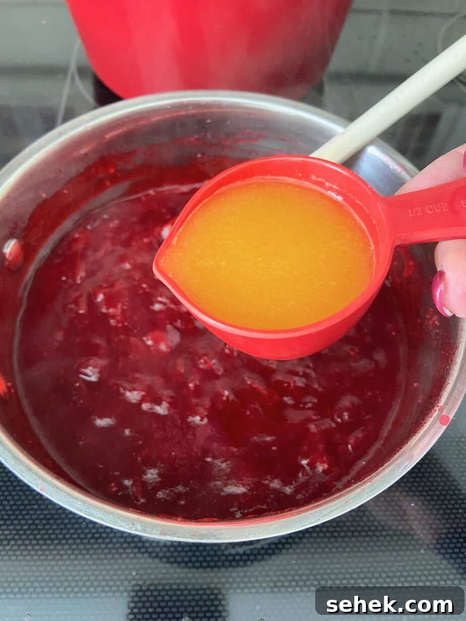 Homemade Spiced Cranberry Sauce with Warm Holiday Spices 5 Orange juice being added to saucepan.