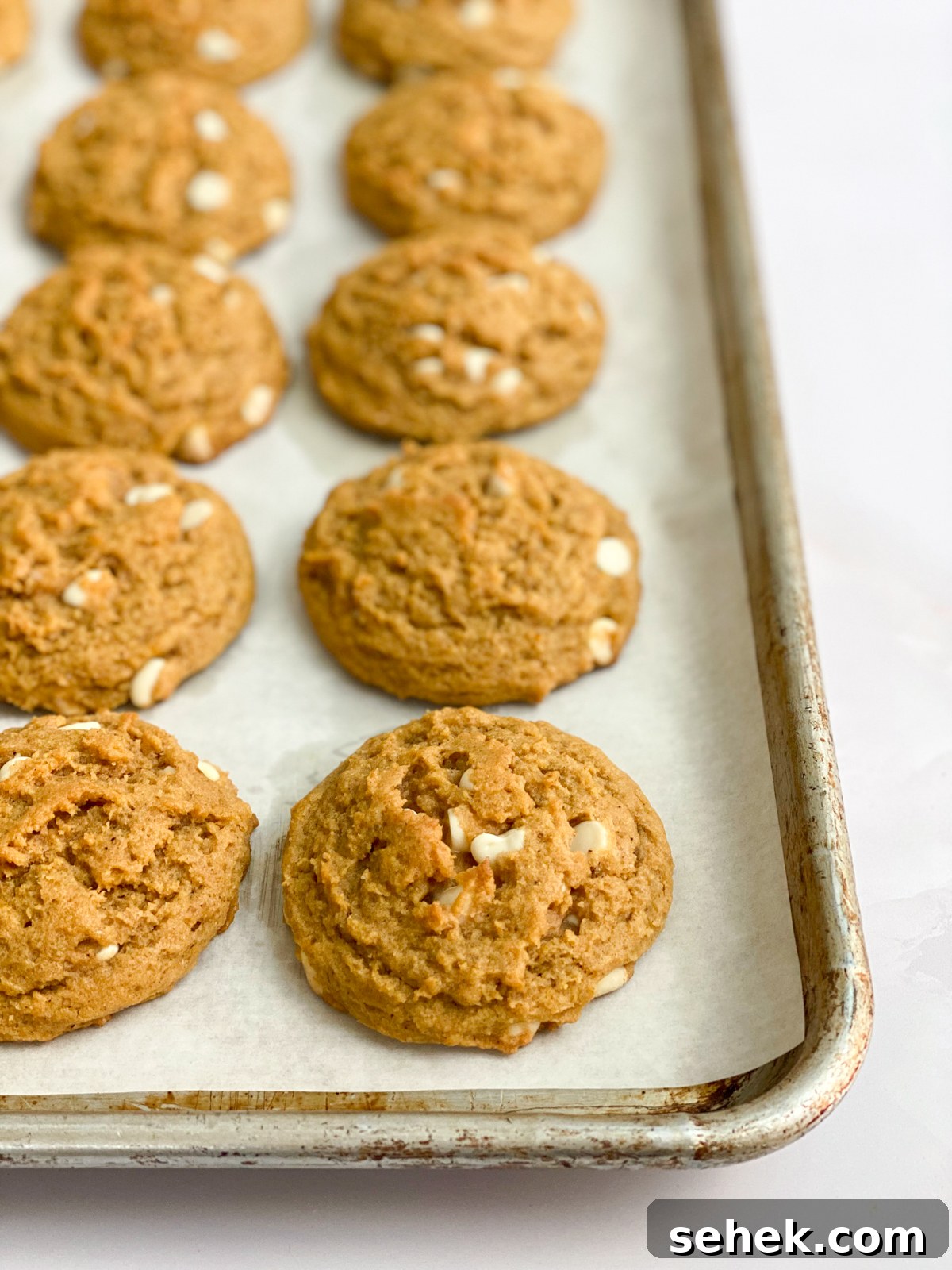 side view of pumpkin white chocolate chip cookies on a baking sheet.