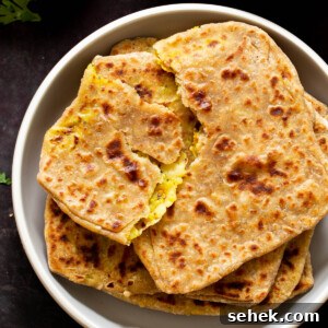 aloo paratha pilled up on a plate, top one is torn open, so you can see the filling