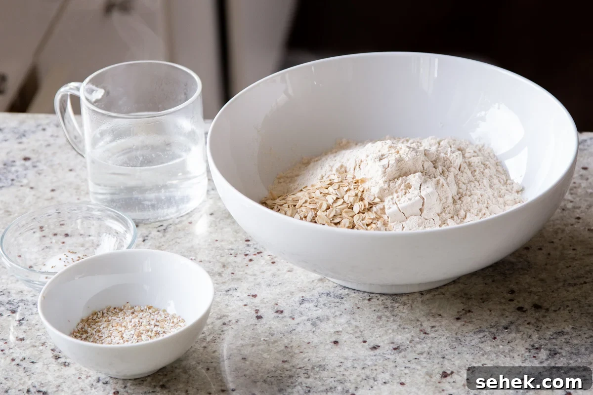 flour and whole grains in a white mixing bowl next to a bowl of buckwheat and a cup of warm water