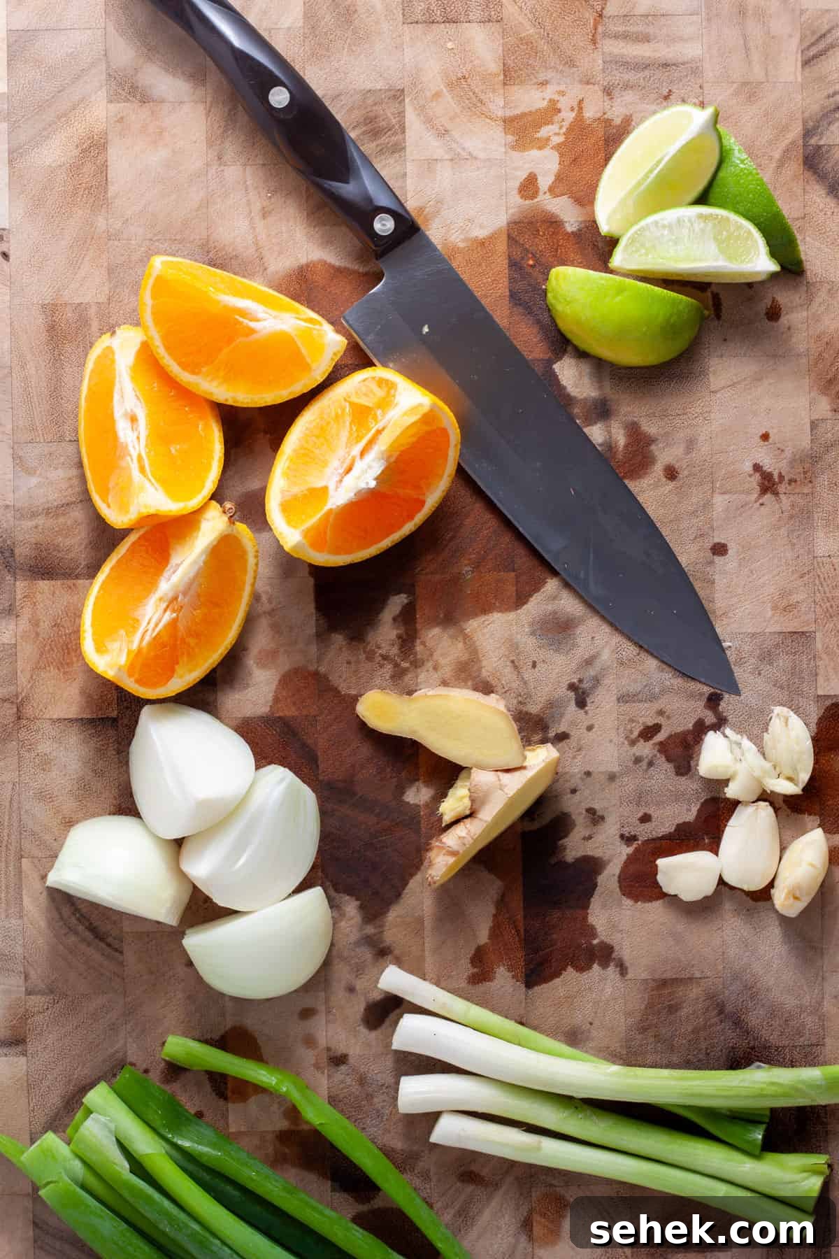 Scallions, ginger, garlic, orange, lime and onion chopped up on a cutting board.
