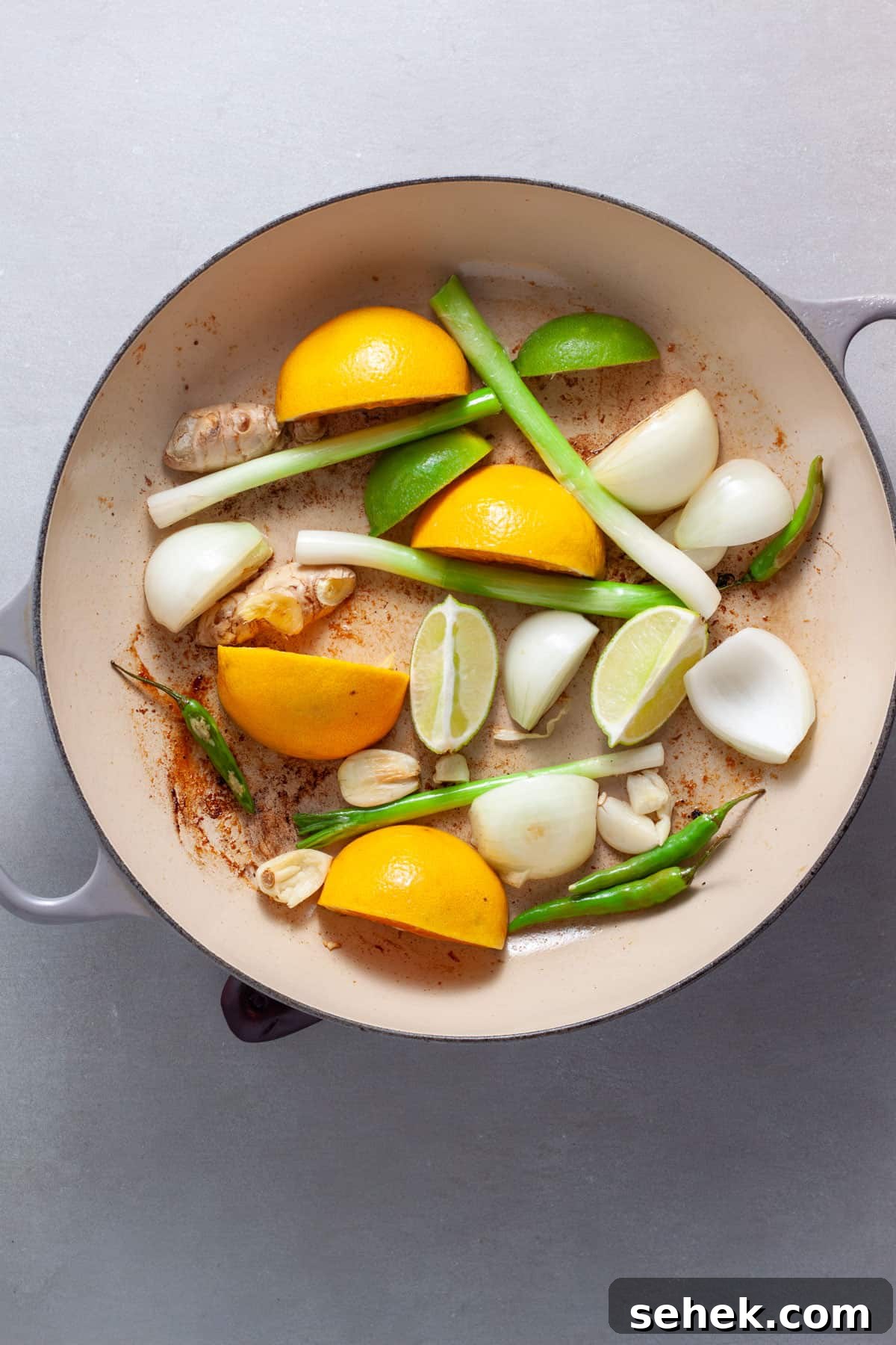 Scallions, citrus, ginger, onion and garlic in a skillet cooking.