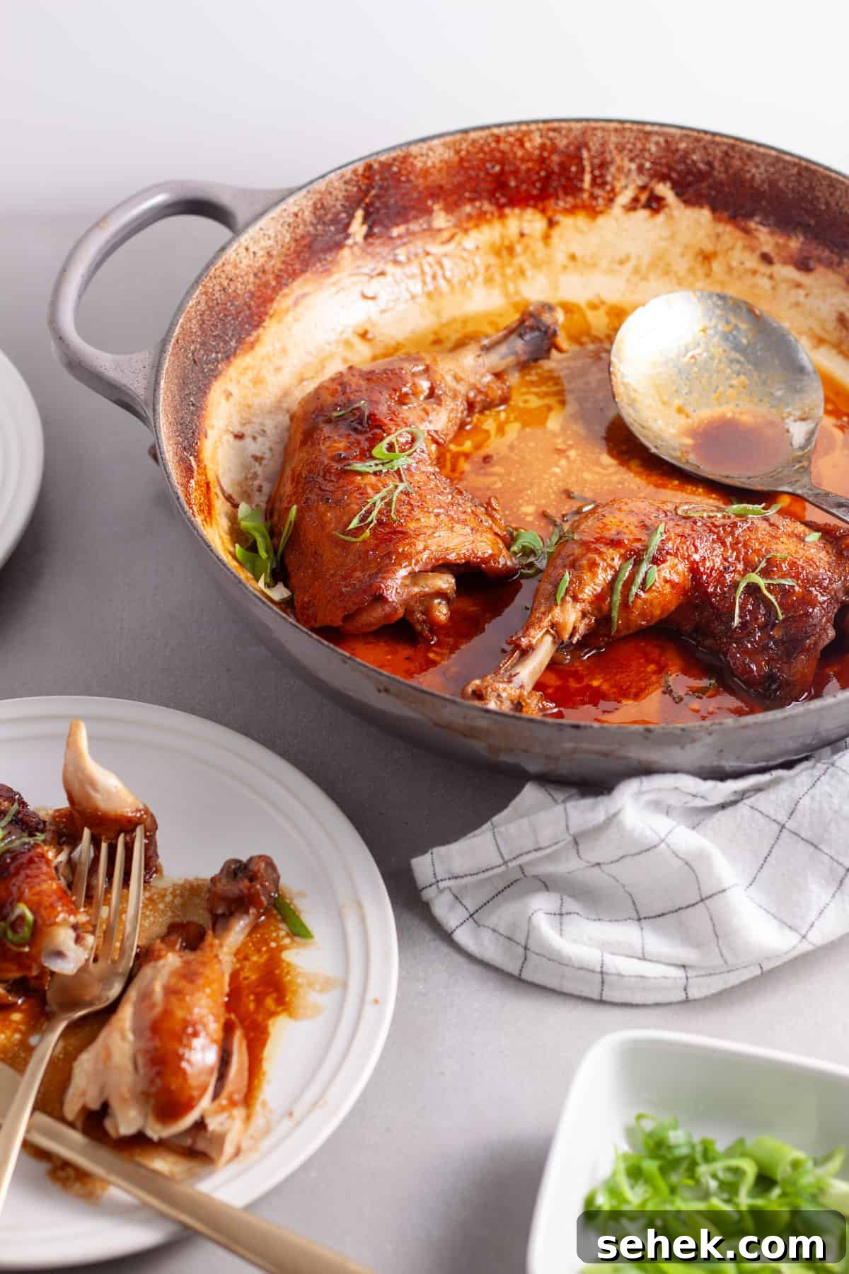 A pot of spicy chicken in a ginger, citrus and soy sauce on a gray table.