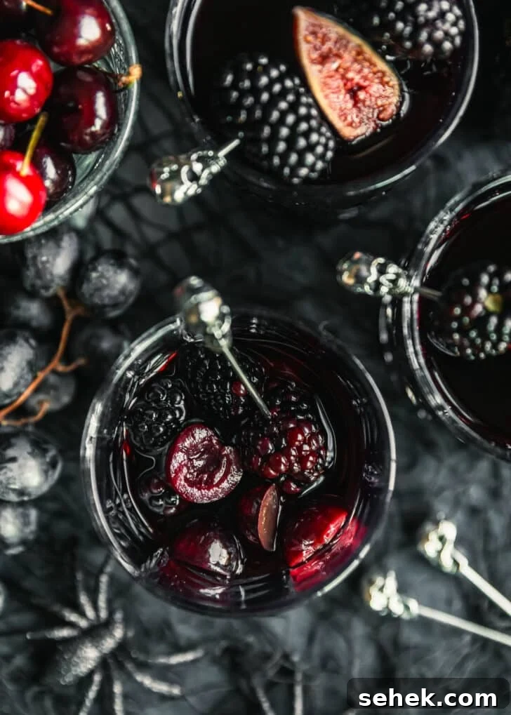 Black Halloween Sangria Recipe with Spooky Blackberry Twist 6 Glasses of black Halloween sangria on a black background next to a bowl of cherries, grapes, and skull cocktail picks.