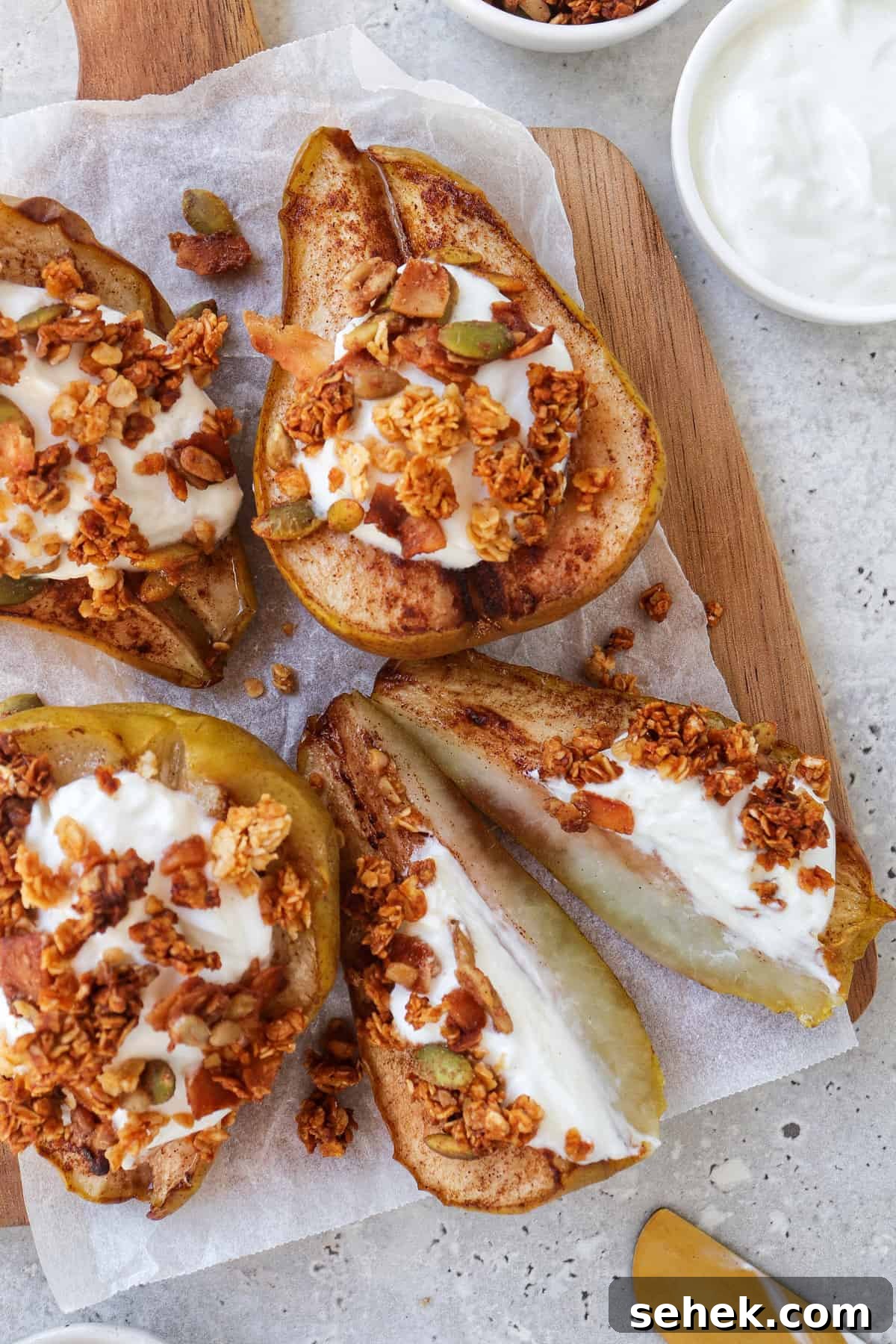 Crispy Cinnamon Air Fryer Pears with Honey Glaze 3 close up shot of baked pears on wooden board topped with plain yoghurt and granola. One pear cut in half.