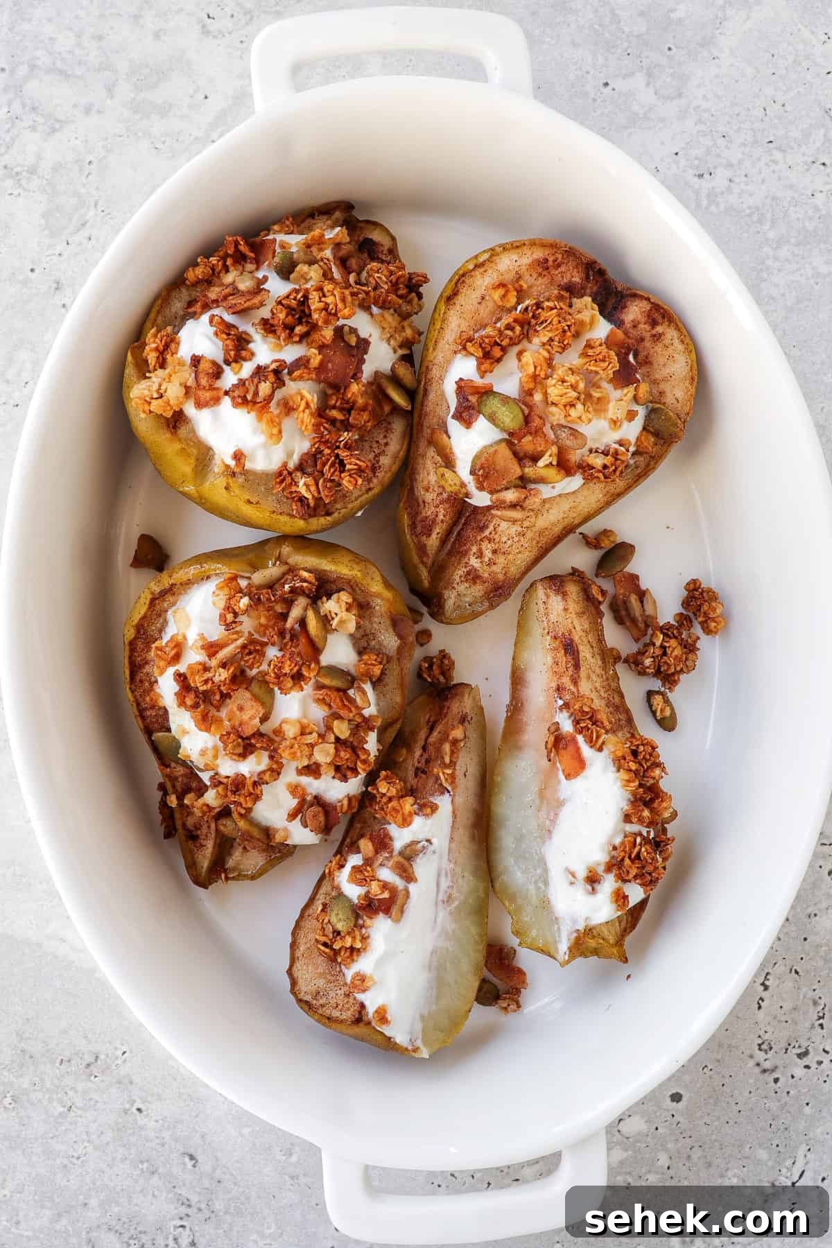 Crispy Cinnamon Air Fryer Pears with Honey Glaze 7 Cooked pears in a white oval dish topped with greek yoghurt and sprinkle of granola.
