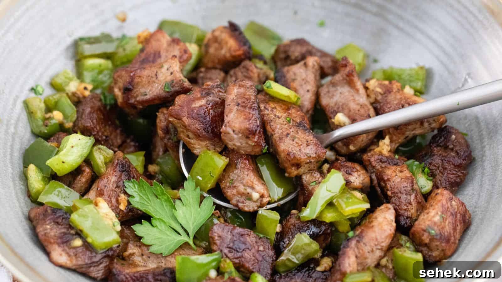 A bowl of meat and green peppers with a spoon.