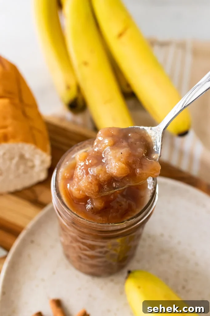 a silver spoon shown lifting a scoop of banana rum jam out of a glass jar