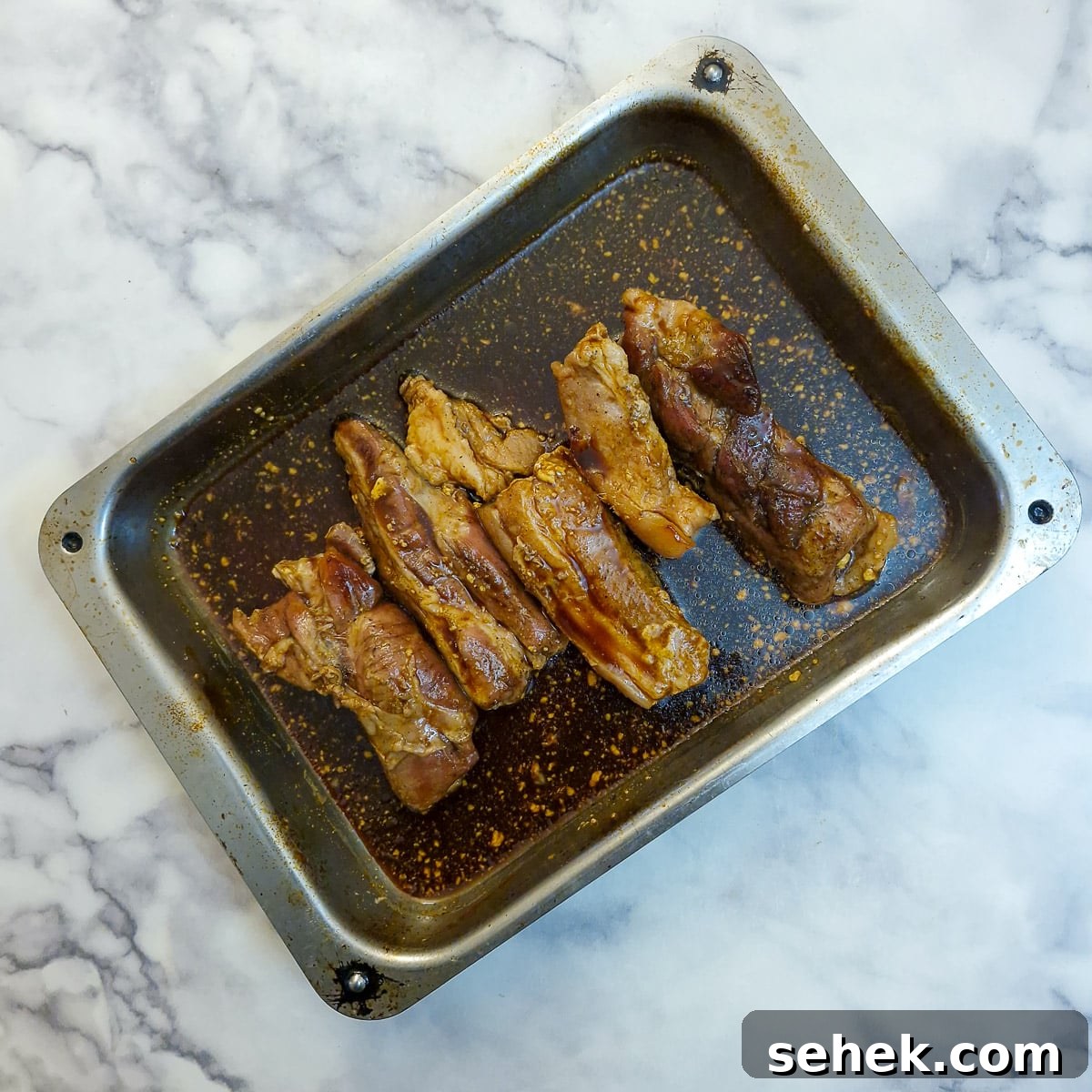 Pork belly slices covered in glaze in a roasting pan.