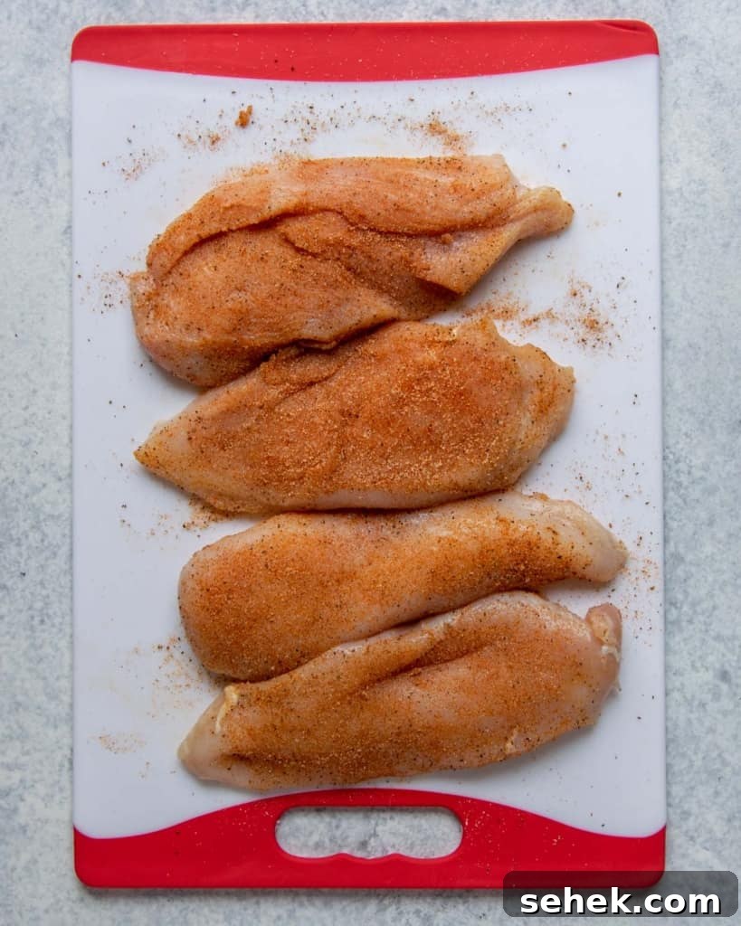 Creamy Dijon Chicken with Mushrooms and Garlic Herbs 5 seasoned raw chicken breast on a white and red cutting board
