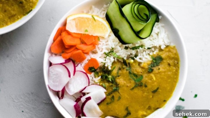 A white bowl filled with Instant Pot Red Lentil Dal, Basmati rice, ribbon of cucumber, sliced carrots and radishes and a lemon wedge.