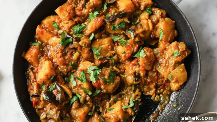 Aloo Baingan in a skillet with naan and yogurt on the side