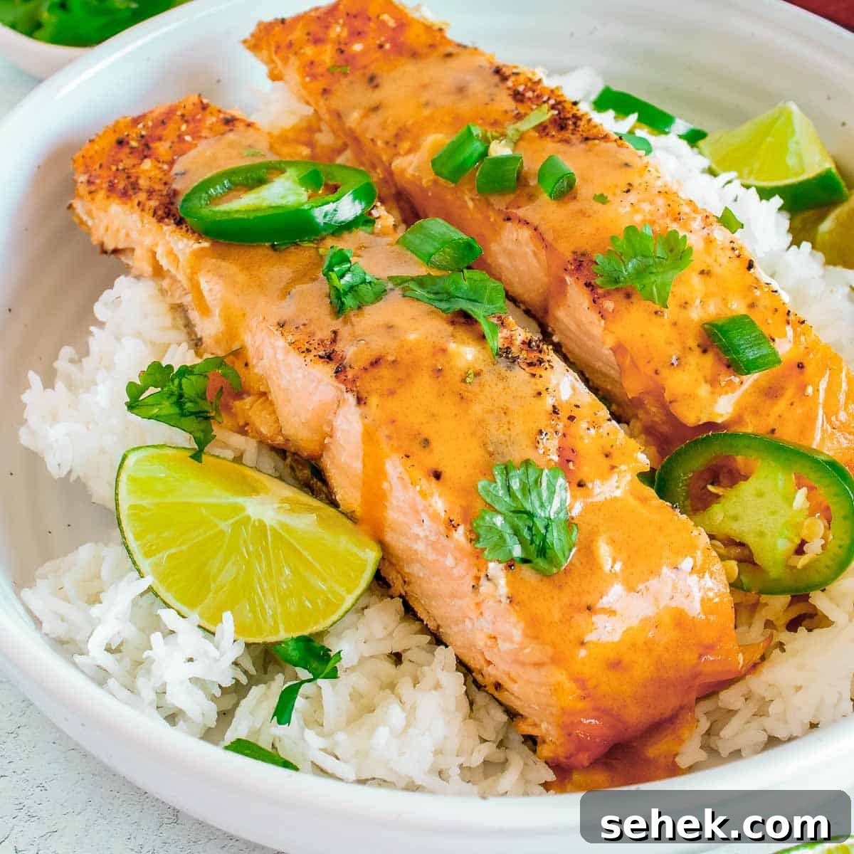 Affordable Seafood Recipes for Flavorful Weeknight Meals 4 Side close up shot of two pieces of salmon on a bed of rice garnished with parsley and cut jalapeños in a large white bowl with lime wedges on the side.