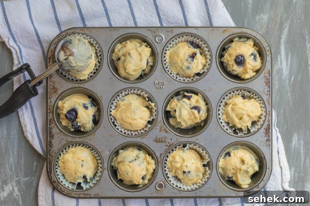 Lemon-Infused Blueberry Muffins Recipe 8 muffin batter being scooped into a muffin tin