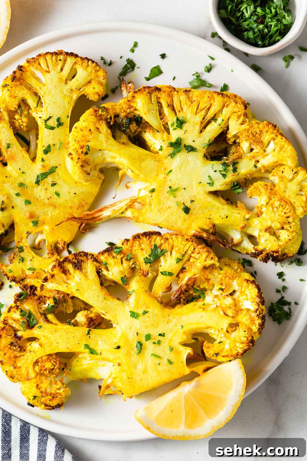 Crispy Air Fryer Cauliflower Steaks with Garlic Herb Sauce 2 air fryer cauliflower steaks with parsley and lemon wedges on a plate.