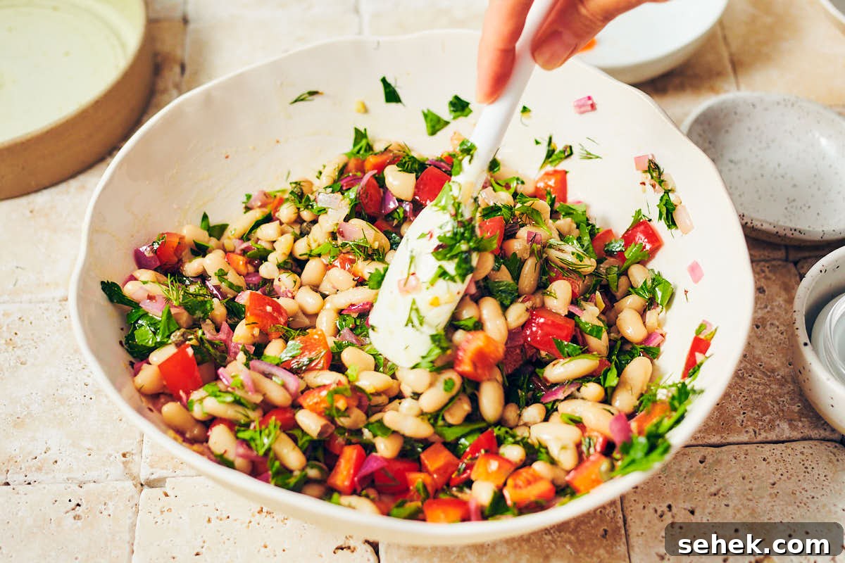 Tuscan Bean Salad with Tomatoes, Olives & Fresh Herbs 5 Stirring together ingredients for Tuscan Bean Salad in a serving bowl.