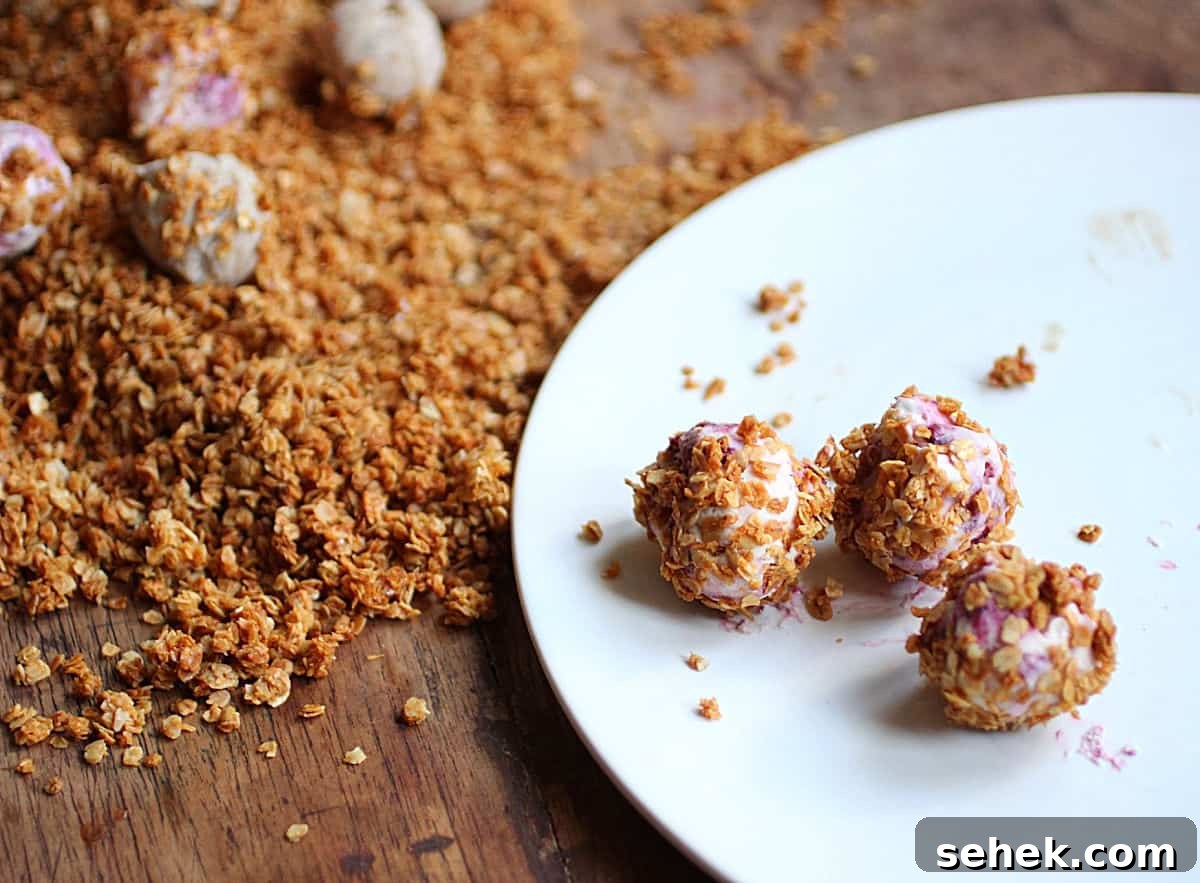 Ice Cream–Filled Granola Truffles: No-Bake Dessert Bites 5 Three granola ice cream truffles in white plate, mound of granola, wooden table.