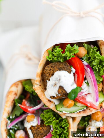 Three vegetable gyros stacked on top of each other and wrapped in white parchment paper.