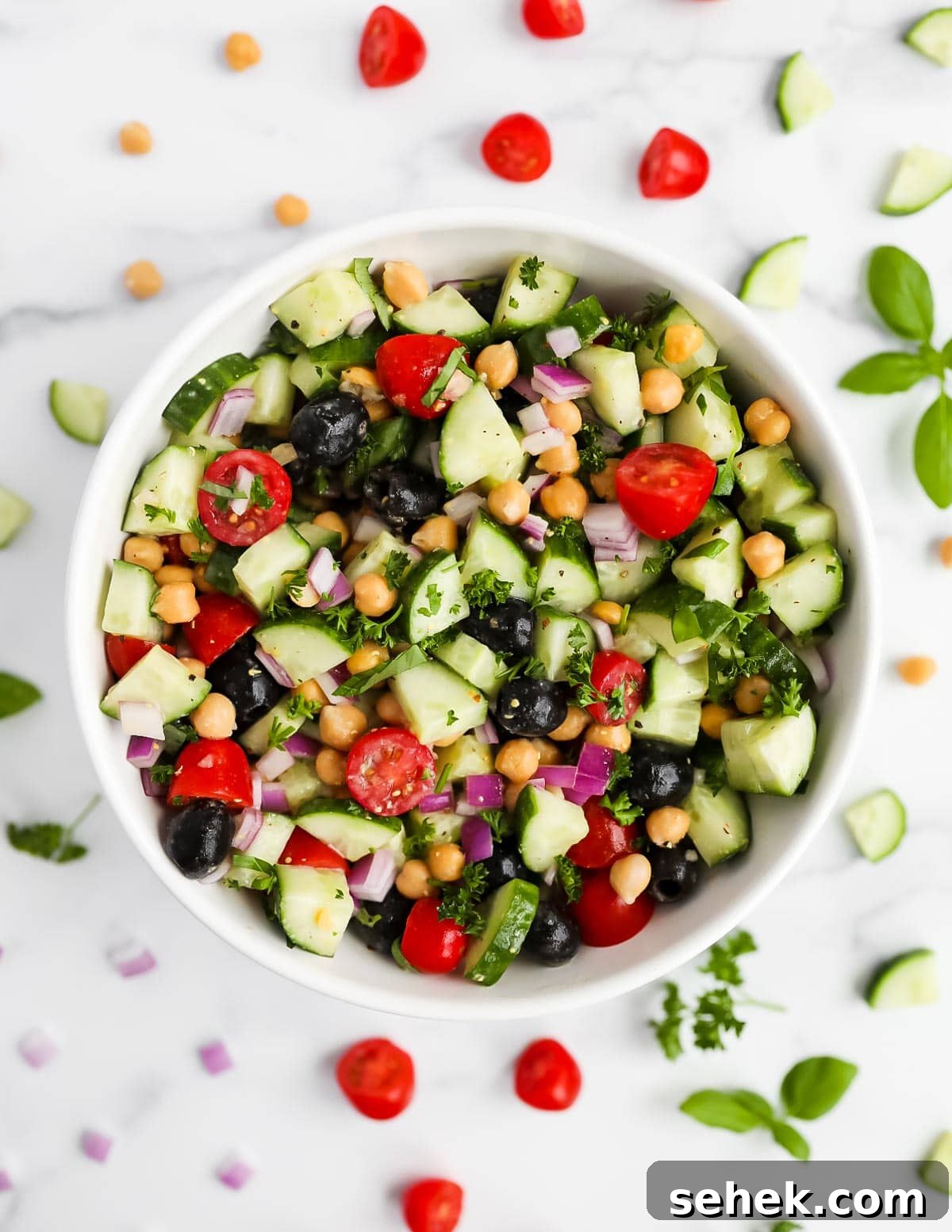 Classic Greek Cucumber Salad with Feta and Olives 6 A overhead image of my cucumber salad garnished outside the bowl with tomatoes, chickpeas, cucumbers, onion, and herbs