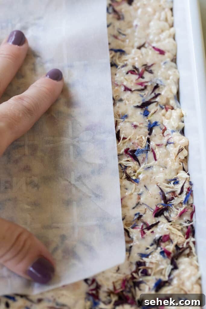 pressing parchment paper down on rice Krispie treat to get an even layer.