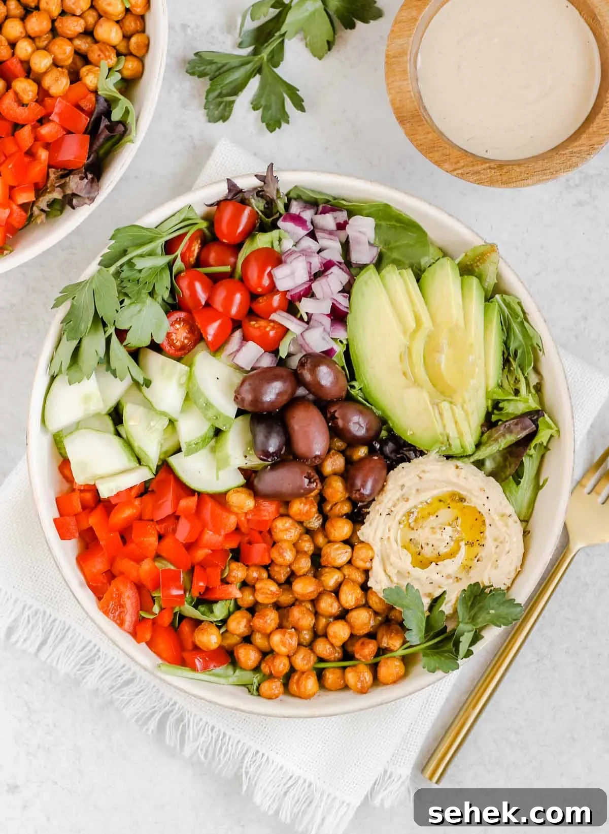 Mediterranean salad in a white bowl with a gold fork and a side of tahini dressing.