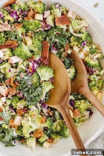 Broccoli salad with kale and red cabbage in a large serving bowl with wooden salad utensils in the bowl.