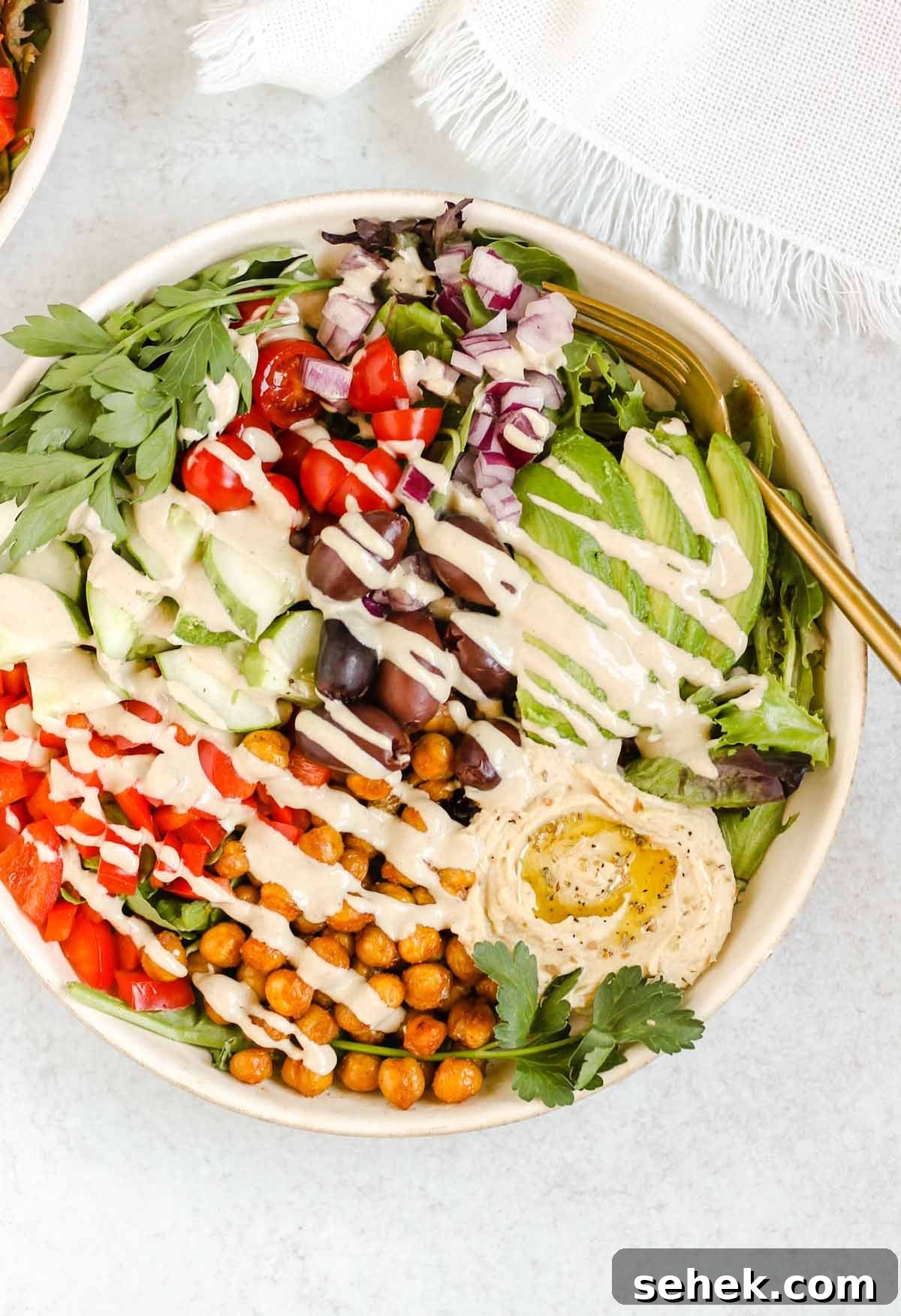 Mediterranean salad bowl with tahini dressing drizzled on top.
