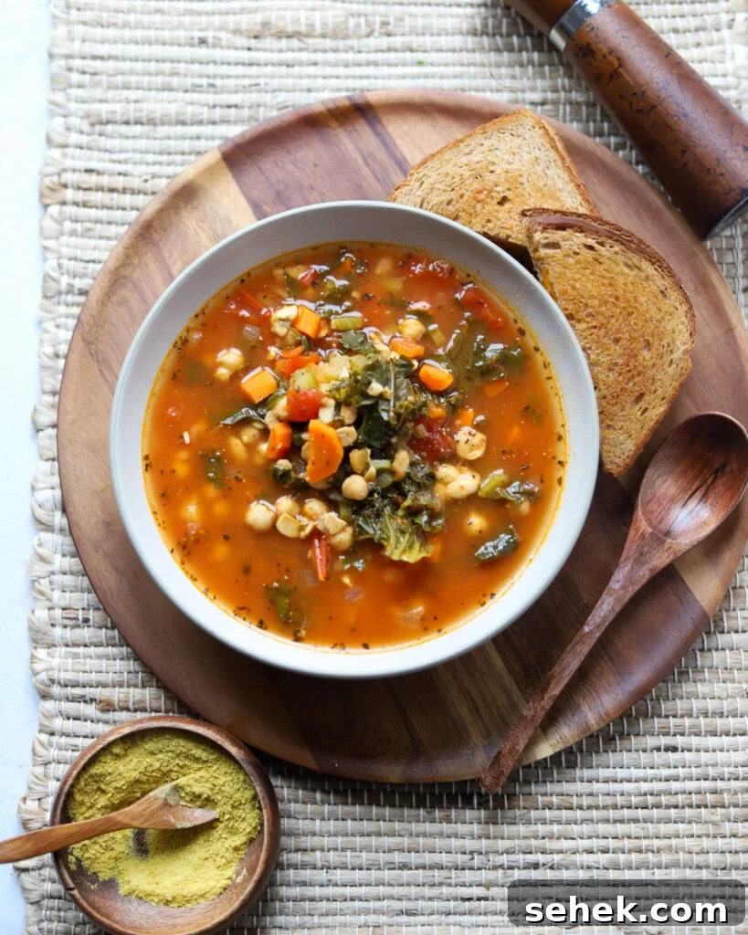 overhead view of a white bowl with vegan sausage kale soup made with tempeh next to toast and a wooden spoon.