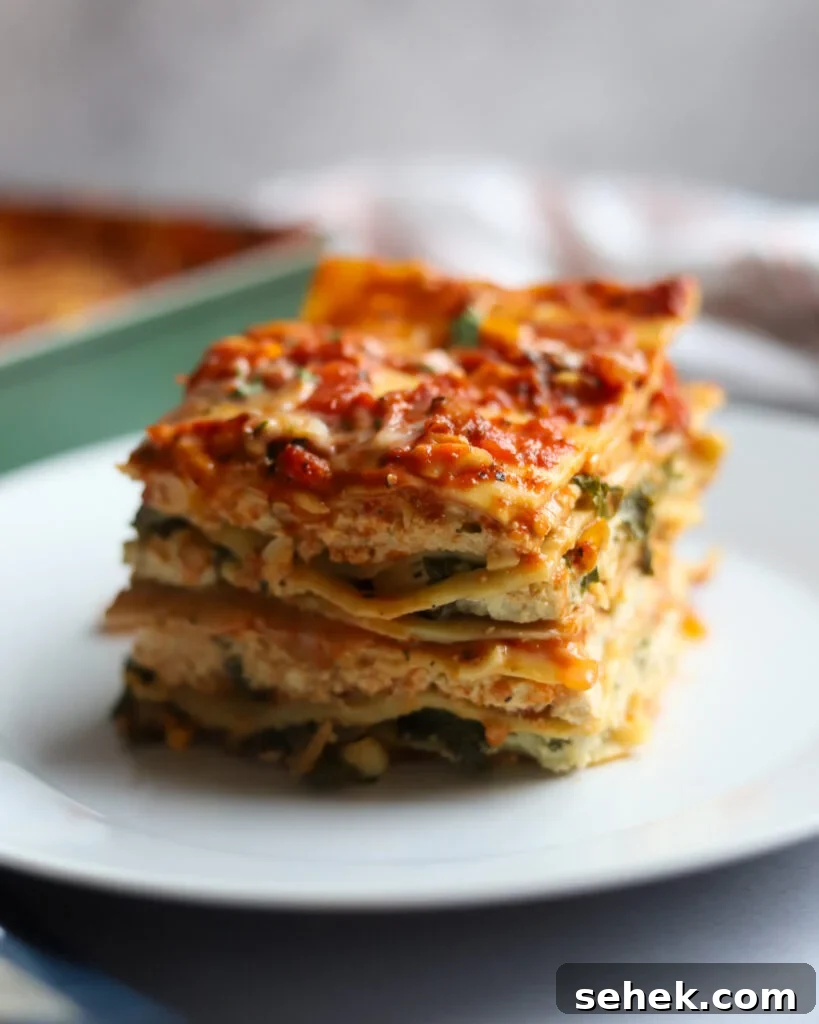 slice of cheesy vegan lasagna with tofu ricotta on a white plate.