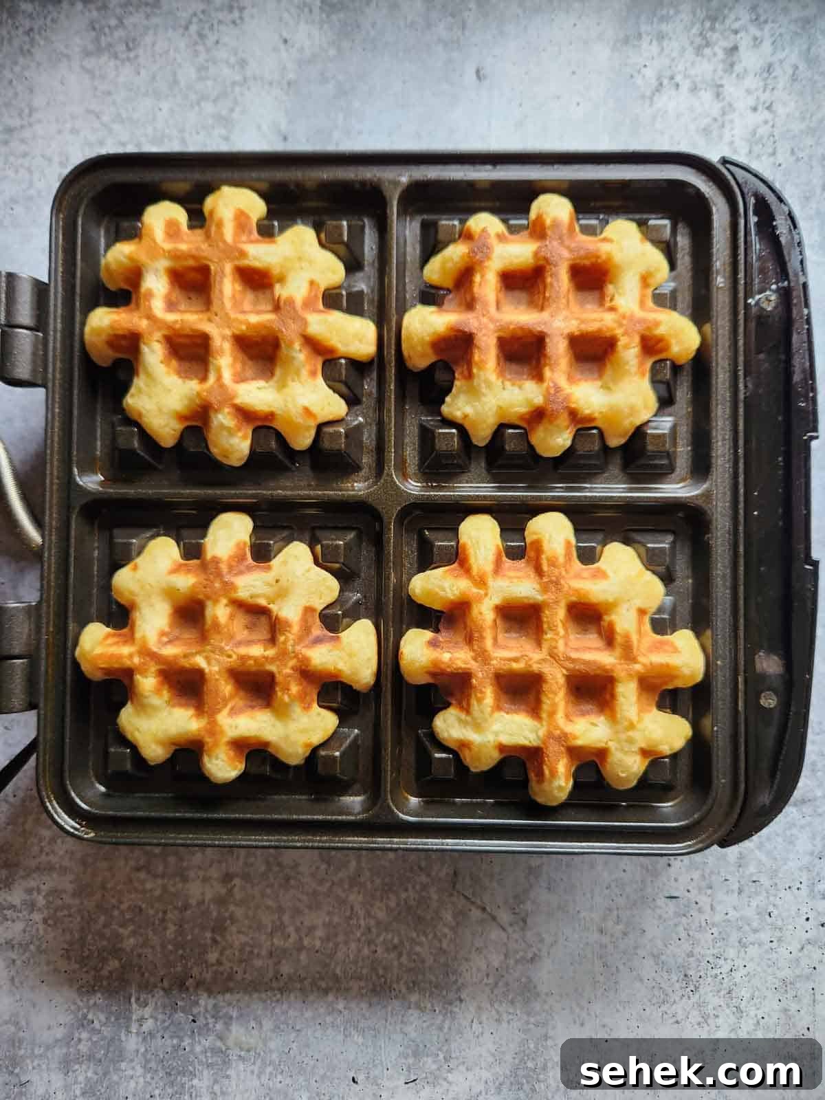 Spiced Eggnog Waffles with Warm Holiday Flavors 9 Four cooked waffles on a waffle maker.