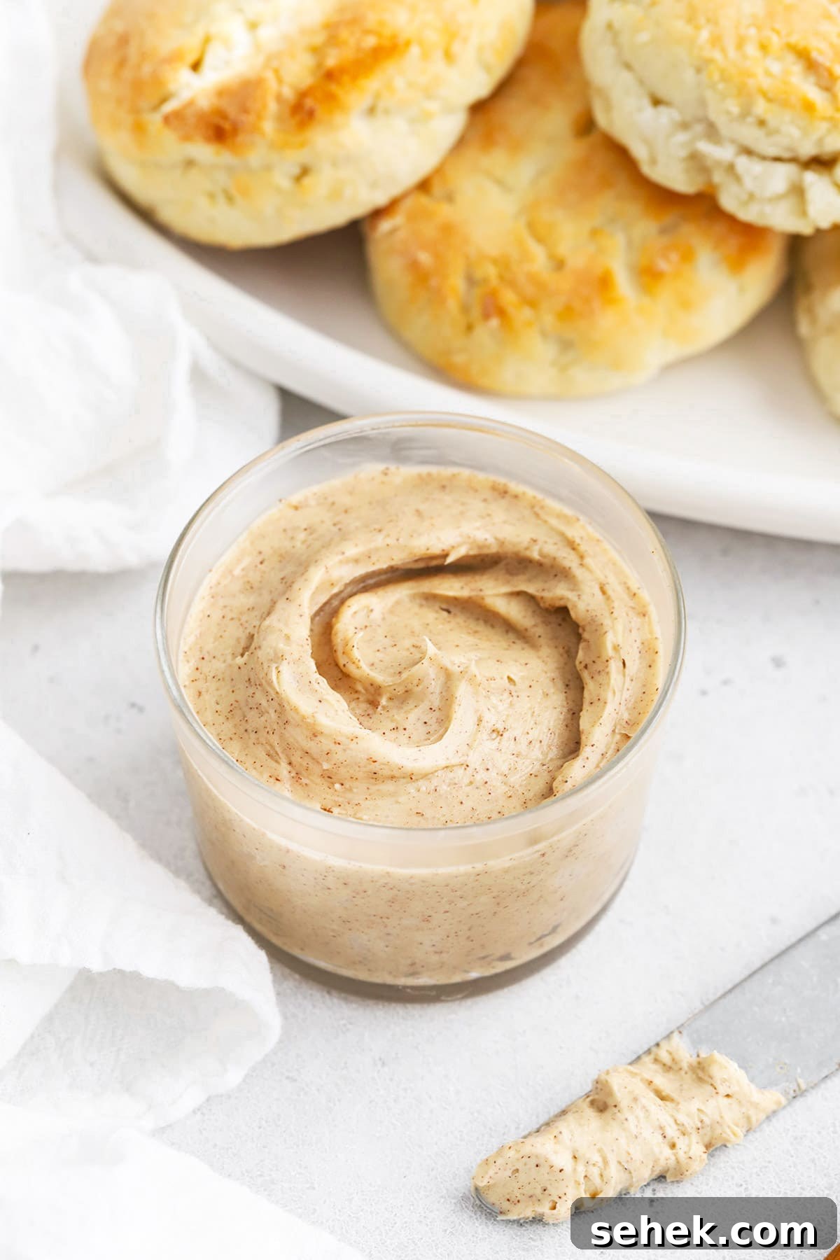 Whipped Honey Butter with Cinnamon — Fluffy Spread Recipe 3 Front view of whipped honey butter in a small glass jar with gluten-free biscuits in the background