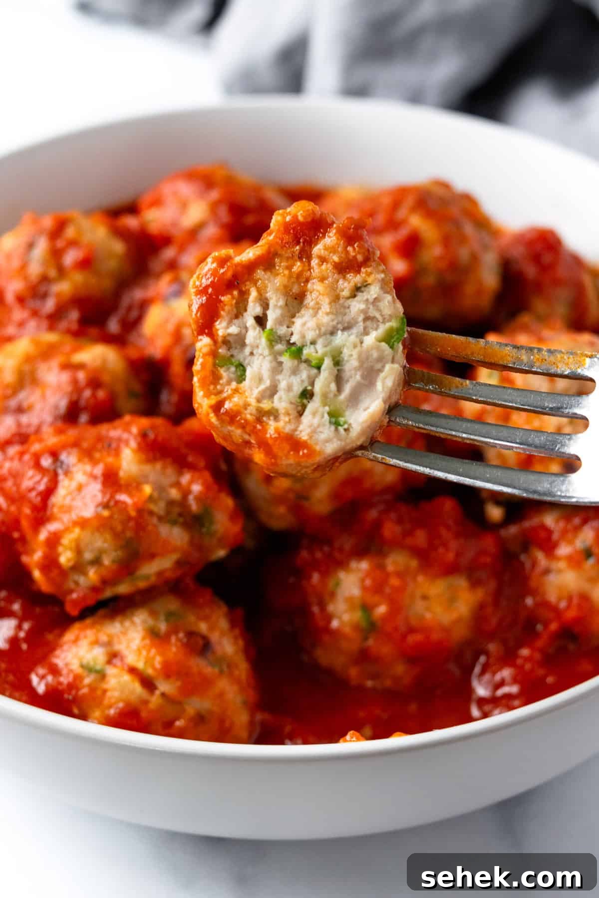 Fork with a turkey zucchini meatball with marinara with a bite missing.