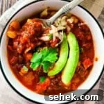 Smoked Brisket and Bean Chili Recipe for Flavorful Comfort 9 Smoked brisket chili topped with avocado, shredded cheese, and onions in a white bowl with a spoon lifting a hearty bite.