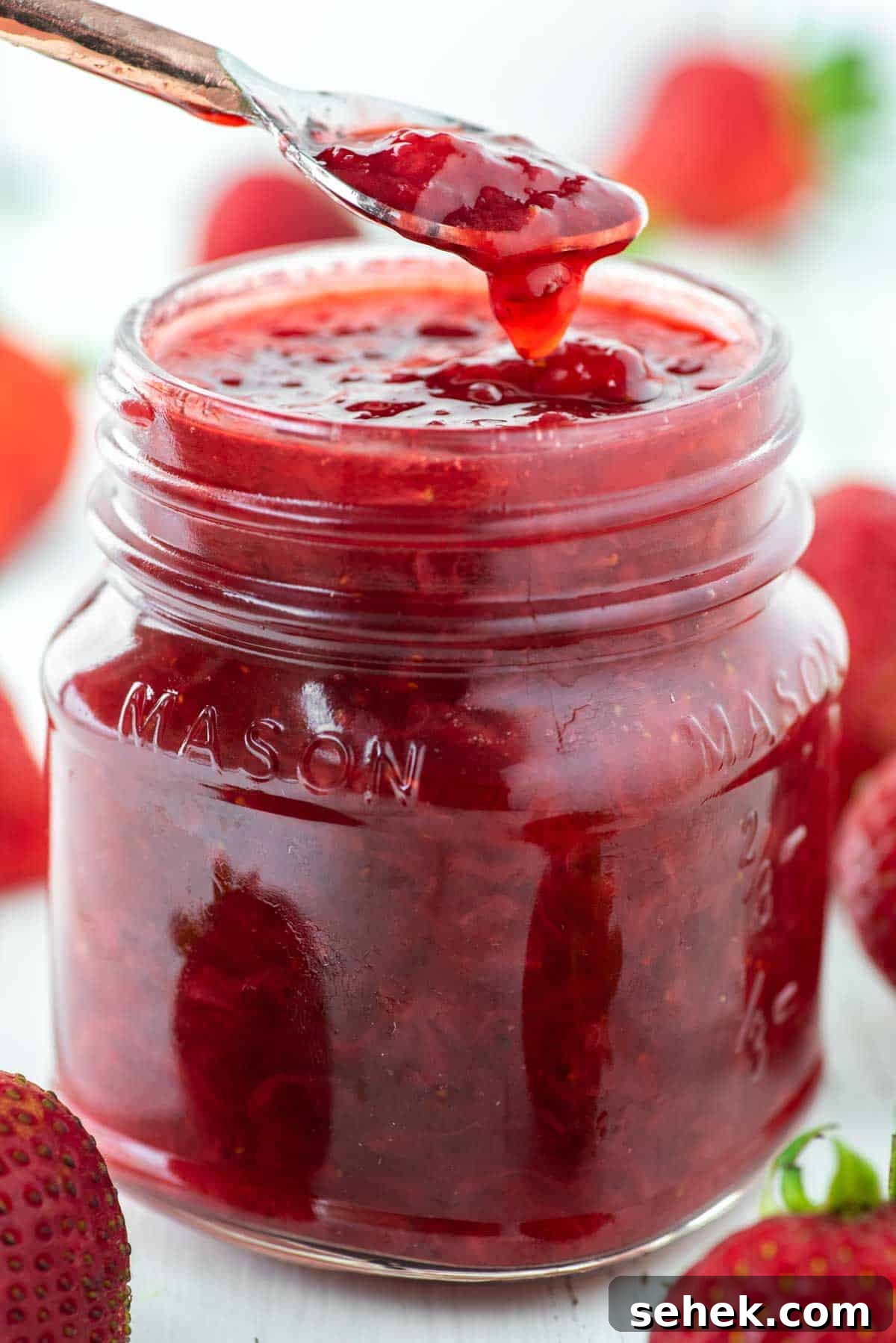Low-Sugar Strawberry Jam Recipe — Small-Batch Preserving Tips 2 Spoon dipped in low sugar strawberry jam in mason jar.