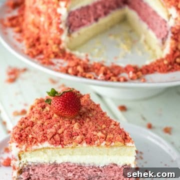 slice of strawberry crunch cake on white plate with rest of cake on cake stand