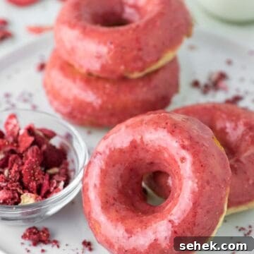 4 strawberry frosted donuts on white plate.