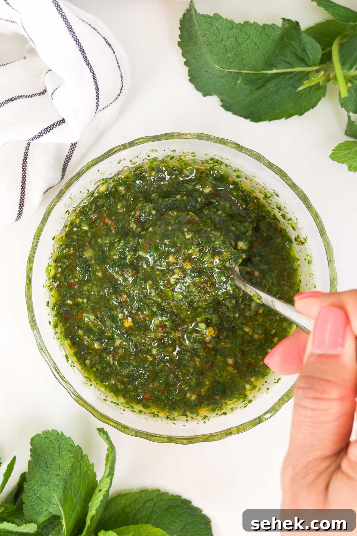 Marinated Grilled Lamb Chops Recipe for Juicy, Flavorful Results 3 overhead of a hand stirring a bowl of mint chimichurri with a spoon on a stone surface