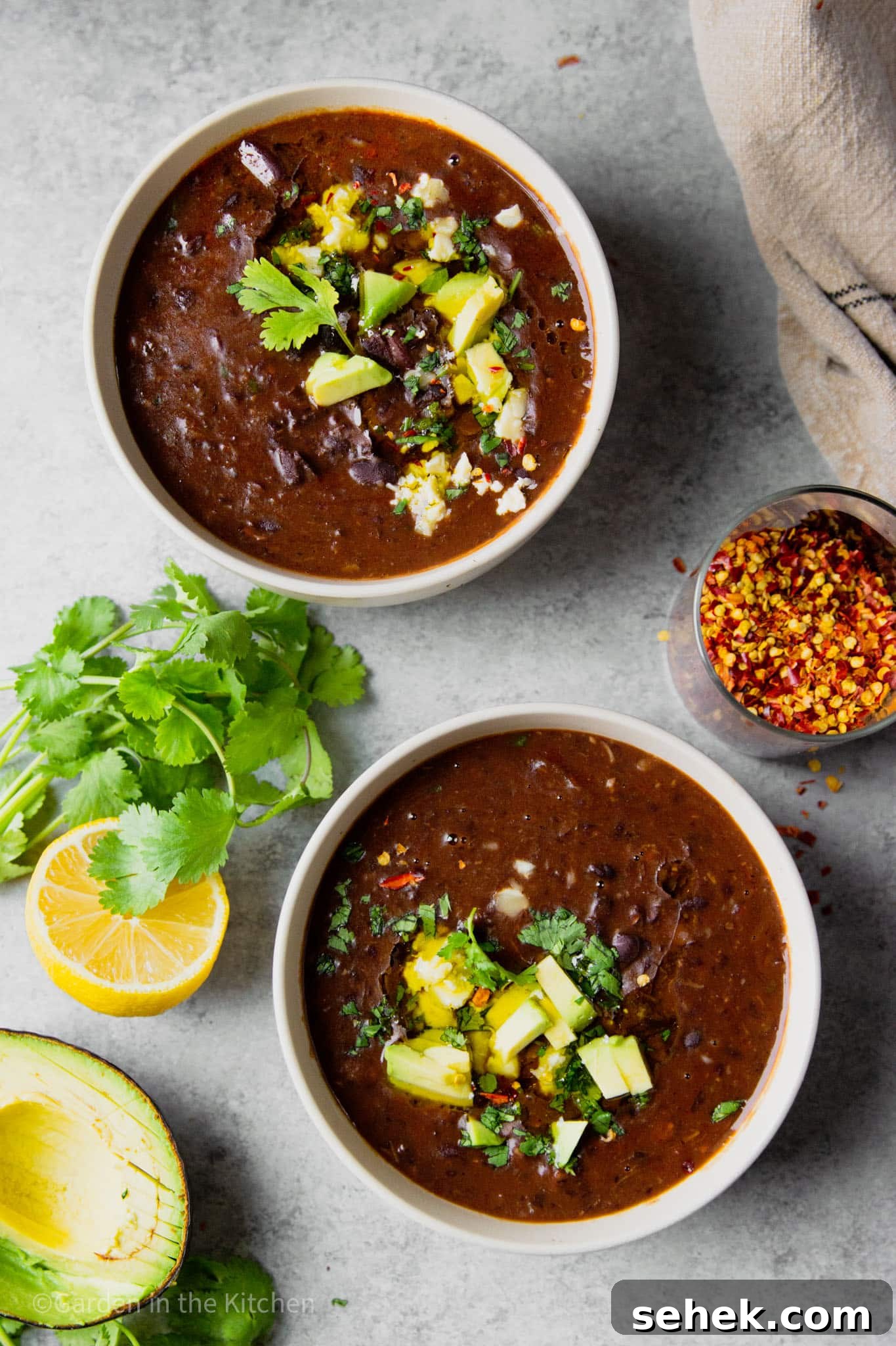 Instant Pot Brazilian Feijoada-Inspired Black Bean Soup 8 2 white bowls of black bean soup topped with avocado and cilantro.